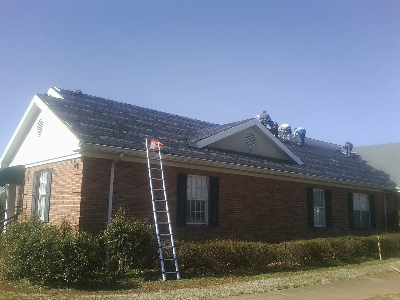 Crew tearing shingles off a brick ranch roof with a ladder set — Metal Roof Repair work by our crew in Pacolet Mills