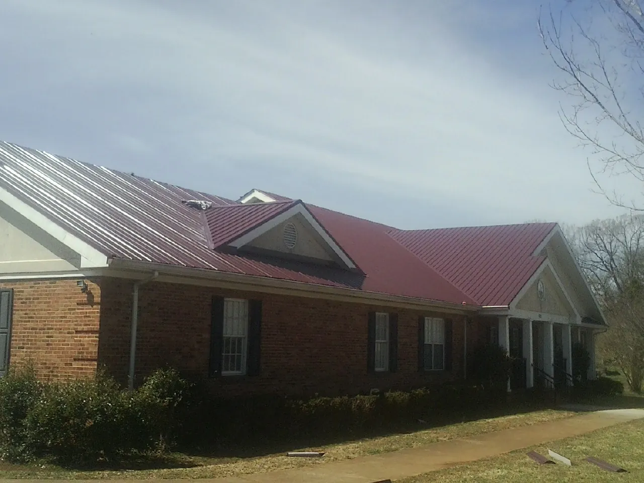 Red metal roof with gabled entries on a long brick building, from a Hail Damage Roof Repair job in Pacolet Mills