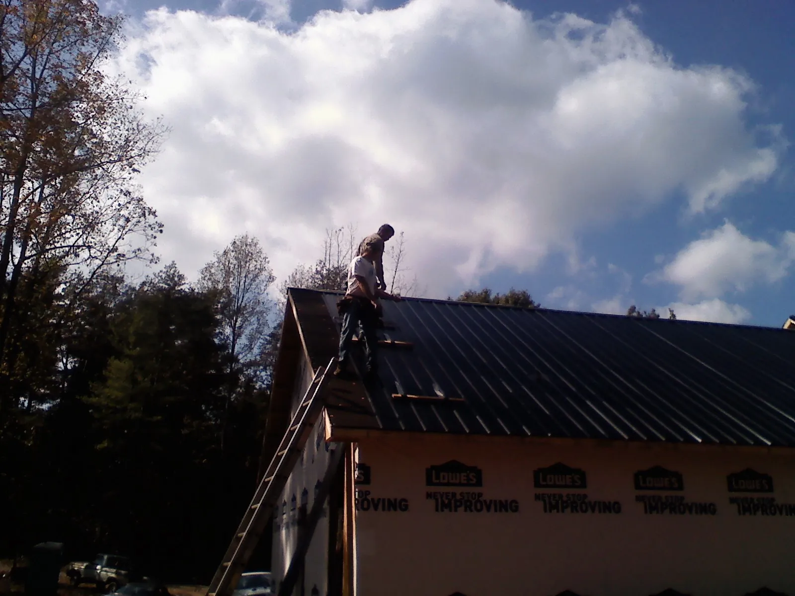Roofer fastening dark metal panels high against a cloudy sky, from a Roof Inspection job in Pacolet Mills