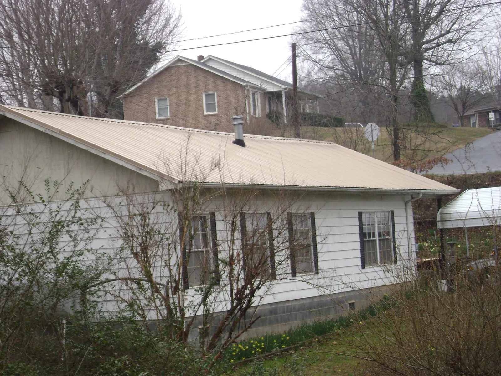 Tan metal roof on a white sided house set into a hillside — Commercial Roofing by Roofing Brothers in Pacolet Mills